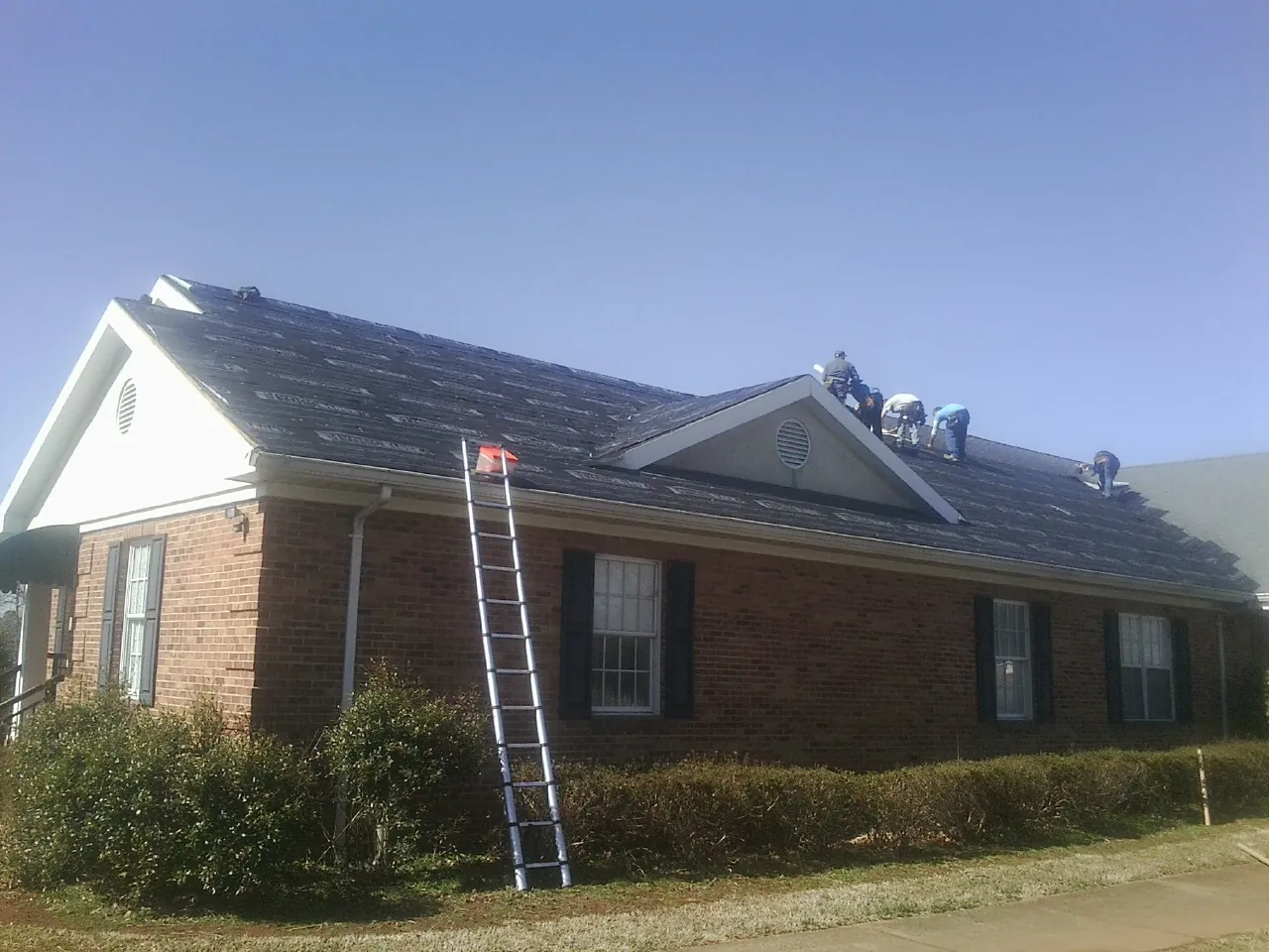 Crew tearing shingles off a brick ranch roof with a ladder set — Emergency Roof Repair work by our crew in Highwood