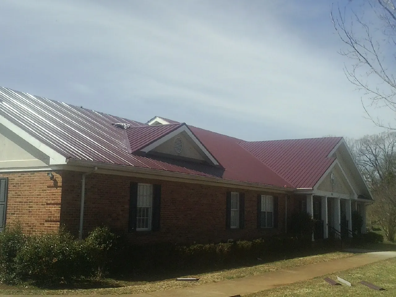 Red metal roof with gabled entries on a long brick building, from a Hail Damage Roof Repair job in Highwood
