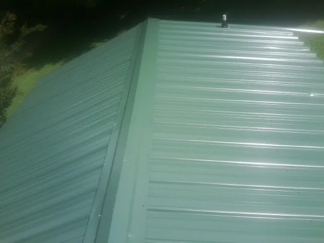 New green metal panels meeting at the ridge of a roof — Flat Roof Repair work by our crew in Highwood