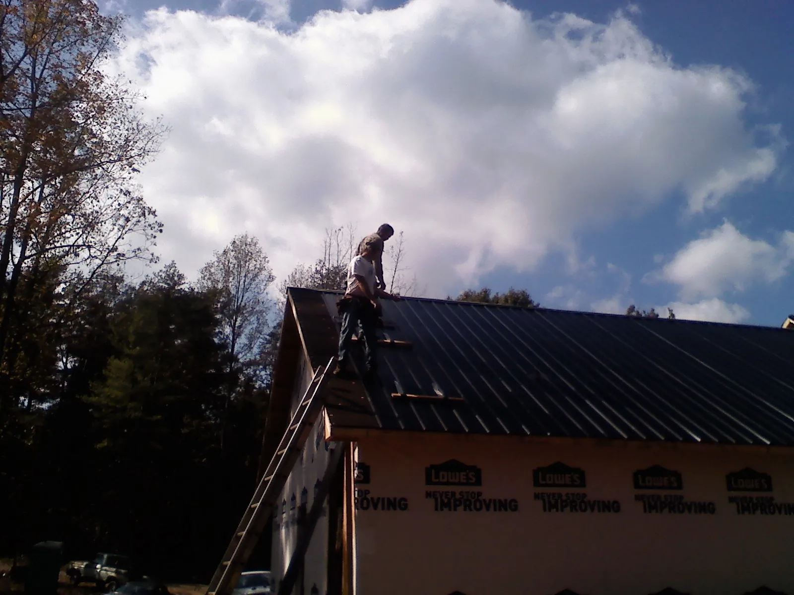 Roofer fastening dark metal panels high against a cloudy sky, from a Roof Inspection job in Highwood