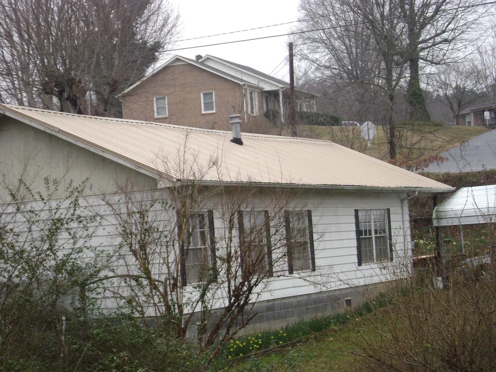 Tan metal roof on a white sided house set into a hillside — Commercial Roofing by Roofing Brothers in Highwood